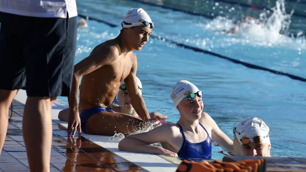 Coach aan de badrand in gesprek met een paar zwemmers aan de kant van het bad